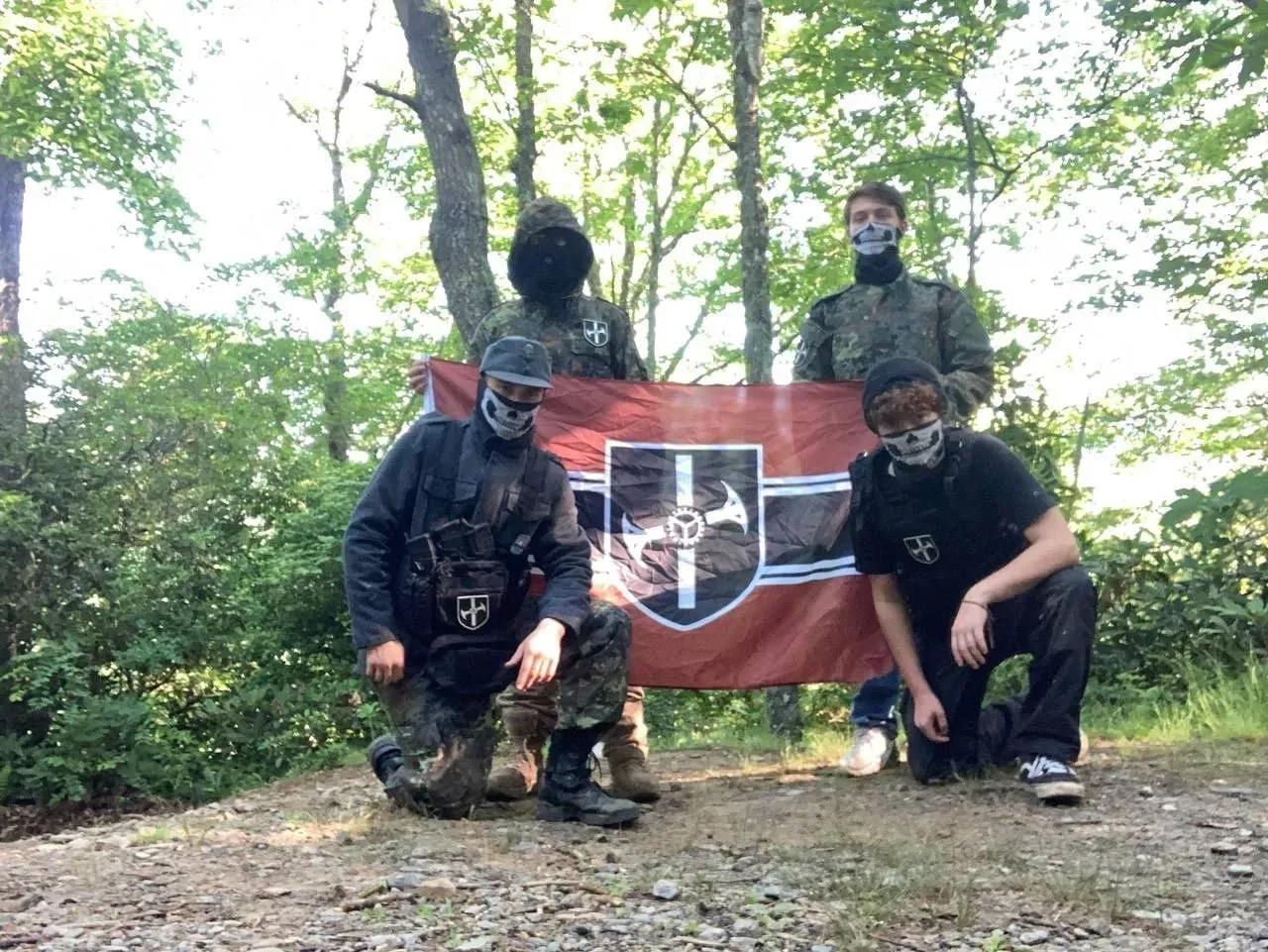 Group photo of four Automata members with the group’s flag. Nary (front row, left) is kneeling in military fatigues and wearing a skull mask and Automata patch (Telegram, June 2021).